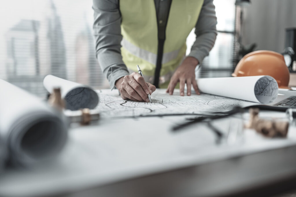 Arbeiter mit Warnweste liest Baupläne auf einem Schreibtisch – Symbol für präzise Tragwerksplanung.